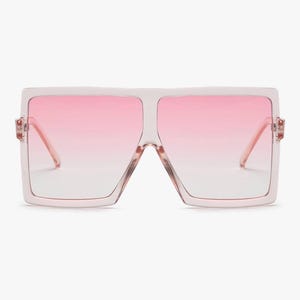 May include: Oversized square sunglasses with a light pink frame and gradient pink lenses. The sunglasses have a bold, modern design, perfect for a fashion-forward look. The lenses transition from a darker pink at the top to a lighter shade at the bottom.