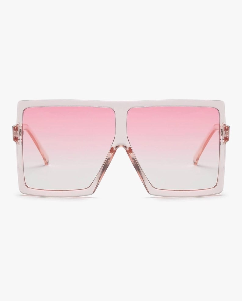 May include: Oversized square sunglasses with a light pink frame and gradient pink lenses. The sunglasses have a bold, modern design, perfect for a fashion-forward look. The lenses transition from a darker pink at the top to a lighter shade at the bottom.