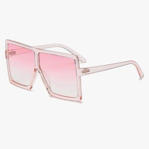 May include: Oversized square sunglasses with a pink gradient lens. The frames and arms are a translucent pink. These fashion sunglasses offer a bold, modern look.