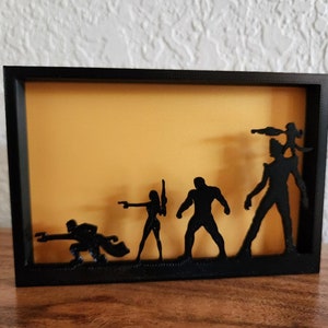 May include: A black frame with a yellow background and five black silhouettes of figures. The figures are arranged in a line from left to right, with the tallest figure on the right and the shortest figure on the left.