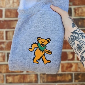 May include: Gray sweatshirt with a yellow dancing bear wearing a green lei.