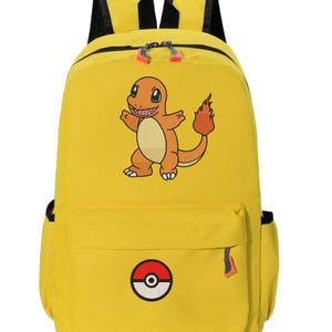 May include: A bright yellow backpack featuring a graphic of the orange lizard-like creature Charmander on the main compartment and a circular red, white, and black Poké Ball emblem centered on the front zippered pocket with black shoulder straps.