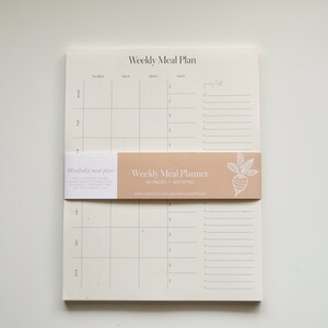 The Weekly Meal Plan notepad lying on a desk. Each Weekly Meal Plan page has space for three meals and two snacks every day of the week and includes a dedicated space for your grocery list.