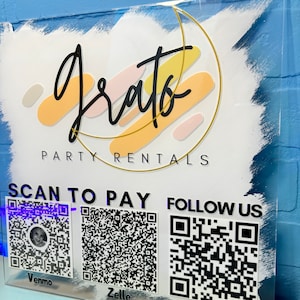 May include: A white acrylic sign with the text "Grato Party Rentals" in black script. The sign has a gold circle with colorful abstract shapes and the text "Scan to Pay" and "Follow Us" with QR codes for Venmo, Zelle, and Instagram.