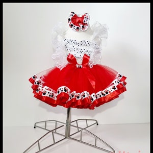 Può includere: Gonna tutu di tulle rosso con pois bianchi e bordatura di nastro di raso rosso. La gonna è abbinata a una camicetta bianca con pois neri e un cerchietto rosso con fiocco con pois neri.