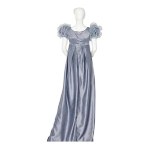 May include: A floor-length, slate blue satin dress featuring a high empire waistline, a scoop neckline, and short, voluminous ruffled sleeves. The back of the garment displays a central vertical seam and pleated fabric that flows down to the floor.