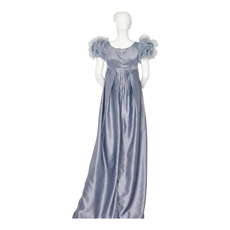 May include: A floor-length, slate blue satin dress featuring a high empire waistline, a scoop neckline, and short, voluminous ruffled sleeves. The back of the garment displays a central vertical seam and pleated fabric that flows down to the floor.
