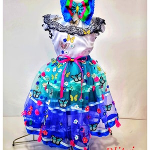 Puede incluir: Una falda de tul de varios niveles en blanco y azul con adornos de mariposas y flores. La falda tiene una cintura de cinta rosa y se combina con una blusa blanca con aplicaciones de mariposas y un lazo azul y verde.