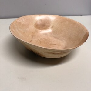 May include: A light brown wooden bowl with a smooth, polished finish. The bowl is made from a single piece of wood and has a natural grain pattern.