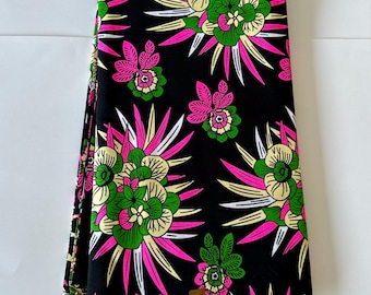May include: Black fabric with a vibrant floral pattern. The design features large flowers in shades of pink, green, and yellow, accented by white and yellow spiky leaves. The fabric is folded and stacked.
