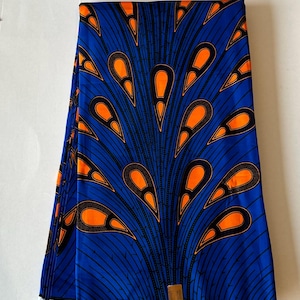 May include: Blue and orange African wax print fabric with a pattern of stylised teardrop shapes. The fabric is folded and has a label that reads "Guaranteed Wax Block Prints Hitard 1404".