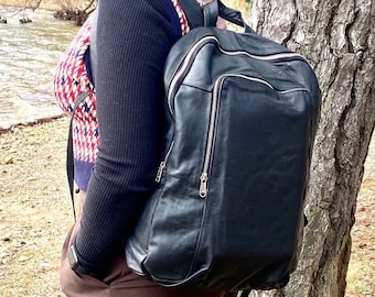 May include: A black leather backpack with silver zippers and a brown belt. The backpack is worn by a person wearing a black sweater and brown pants.