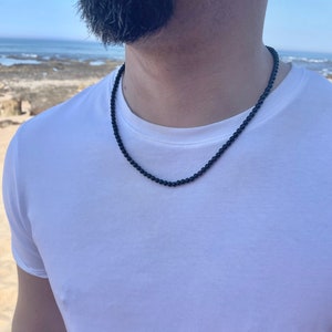 May include: A black beaded necklace worn by a person. The necklace is made of small, round beads and is about 18 inches long.