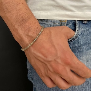 Puede incluir: Una pulsera de cuentas con pequeñas cuentas de color verde claro y detalles plateados. La pulsera se lleva en la muñeca, con una camisa blanca y unos vaqueros azules de fondo. La pulsera parece estar hecha de piedra natural.