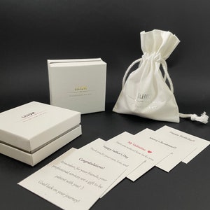 May include: Two white square gift boxes with the text LILIUM Handmade for you, a white drawstring pouch with the same branding, and several white rectangular cards with printed messages including Congratulations, Happy Father's Day, and My Valentine.