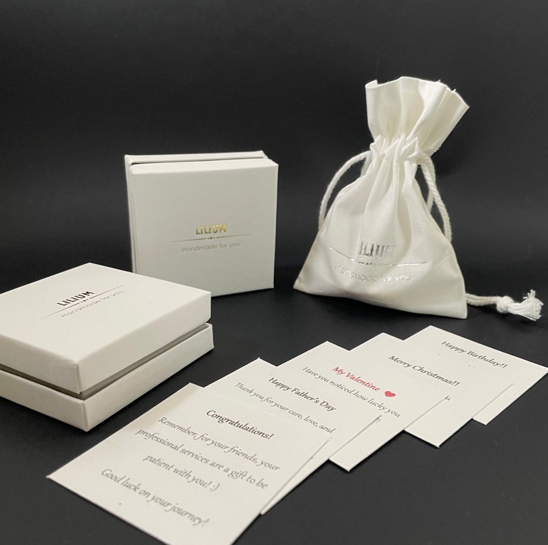 May include: Two white square gift boxes with the text LILIUM Handmade for you, a white drawstring pouch with the same branding, and several white rectangular cards with printed messages including Congratulations, Happy Father's Day, and My Valentine.