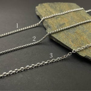May include: Three silver-toned metal chains labeled with numbers one, two, and three. Chain one is a thin curb chain, chain two is a box chain, and chain three is a cable chain. Each chain features a distinct link style and metallic finish.