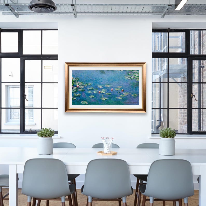 May include: A framed painting of water lilies in a pond. The painting is in a gold frame and is hanging on a white wall. The painting is surrounded by a white wall and a dining table with chairs.
