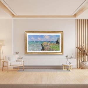 Puede incluir: Una pintura de paisaje enmarcada con un marco dorado representa una escena costera. La obra de arte muestra un acantilado con vistas a un mar turquesa bajo un cielo azul con nubes blancas. Figuras con un paraguas rojo est&aacute;n en el acantilado.