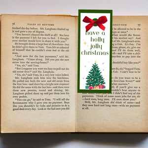 Könnte beinhalten: Ein grünes Lesezeichen mit einer roten Schleife und einer Illustration eines Weihnachtsbaums. Das Lesezeichen trägt den Text "have a holly jolly christmas".