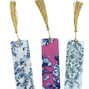 May include: Three rectangular bookmarks with floral patterns and gold tassels. The bookmarks feature designs in blue and white, pink and blue, and green and white. Each bookmark has a gold tassel attached at the top.