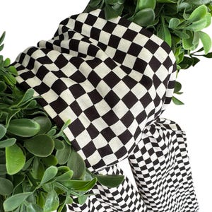 May include: A black and white checkered fabric wreath with green foliage.