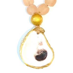 May include: A gold-trimmed oyster shell pendant necklace with a pink glass bead chain. The oyster shell has a natural pearl inside.