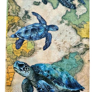 May include: A decorative towel featuring a vintage map design with three blue sea turtles. The turtles are depicted in various sizes and poses, with detailed patterns on their shells. The background has a faded, aged appearance.