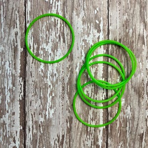 Op de afbeelding: Een stapel felgroene elastiekjes op een verweerd houten oppervlak.