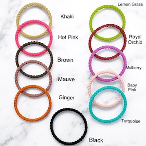 May include: A collection of colorful, braided hair ties in various shades, including khaki, hot pink, brown, mauve, ginger, and black. Additional colors include lemon grass, royal orchid, mulberry, baby pink, and turquoise. Each tie is labeled with its color name.