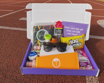 May include: A purple box containing running essentials, including sunglasses, snacks, and a water bottle. The box includes items like a bottle of SIS, a snack labelled BIG, and a card with the text "when your legs get tired, run with your heart."