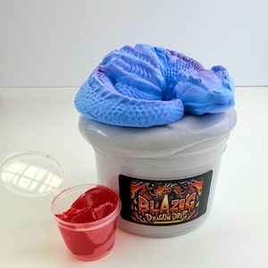 May include: A white plastic container with a blue and purple dragon slime inside. The container has a label that says "Blazing Dragon Drip". There is a small red plastic container with red slime next to it.