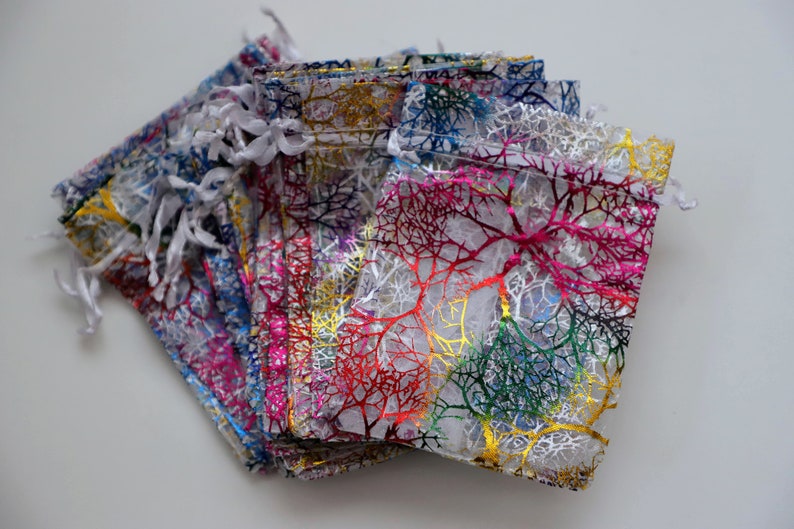 May include: A stack of small, sheer, white gift bags with a colorful, metallic, branch-like pattern. The bags have white drawstrings.