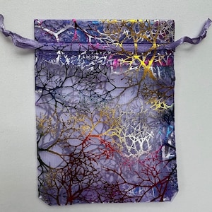 May include: A purple mesh drawstring bag with a colorful tree branch design. The bag is made of sheer fabric and has a metallic sheen.