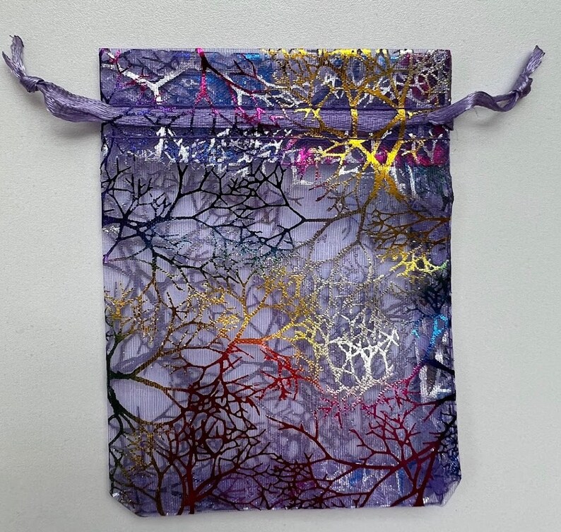 May include: A purple mesh drawstring bag with a colorful tree branch design. The bag is made of sheer fabric and has a metallic sheen.