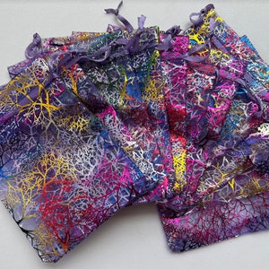 May include: A stack of purple organza gift bags with a colorful leaf design. The bags have a drawstring closure.