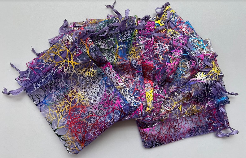 May include: A stack of purple organza gift bags with a colorful leaf design. The bags have a drawstring closure.