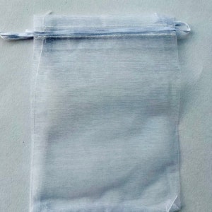 May include: A white sheer drawstring bag made of mesh fabric. The bag is empty and has a white drawstring.
