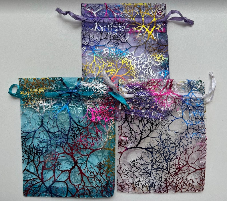 May include: Three sheer fabric gift bags with a tree branch design. The bags are in shades of purple, blue, and white.