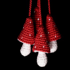 May include: Five red crocheted mushroom ornaments with white stems hanging from white strings against a black background.
