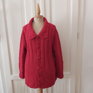 Könnte beinhalten: Ein roter Strickcardigan mit Kragen und Knopfleiste. Der Cardigan hat eine gerippte Struktur und wird auf einer Puppe präsentiert.