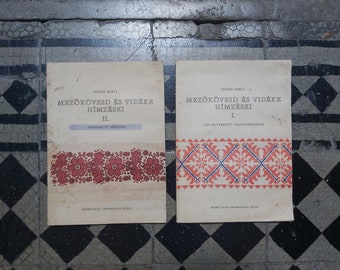 May include: Two vintage books titled "Mezőkövesd és vidéke Hímzései" (Mezőkövesd and its Surroundings Embroidery) with red and blue embroidery designs on the covers. The book on the left is volume II, "Szabályrajzú Hímzések" (Regular Pattern Embroidery), and the book on the right is volume I, "Szálanvarrott Vázsonhímzések" (Thread-Sewn Canvas Embroidery).