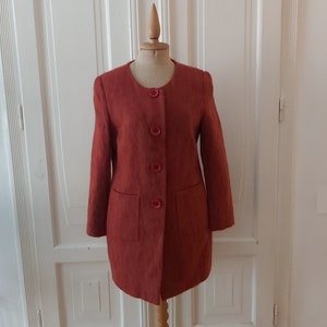 May include: A rust-colored long-sleeved jacket with a round neckline and five buttons down the front. The jacket has two pockets on the front.