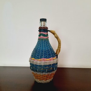 Vintage wicker demijohn bottle. Colorful plastic demijohn bottle. Glass bottle wrapped in colorful plastic wicker. Retro rustic decor.