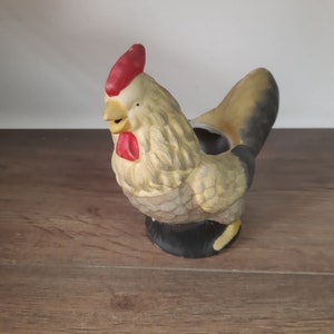 Peut inclure: Un pot de fleurs en c&eacute;ramique en forme de coq avec une cr&ecirc;te et des barbillons rouges, des plumes blanches et une queue noire. Le pot a un trou en haut pour planter.