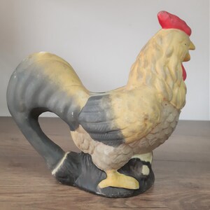 Peut inclure: Une figurine de coq en c&eacute;ramique avec un corps jaune et noir, une cr&ecirc;te rouge et un bec jaune. Le coq est debout sur une surface en bois.