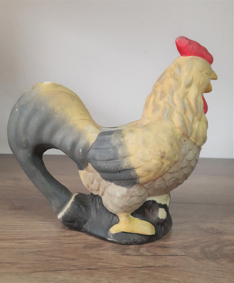 Peut inclure: Une figurine de coq en c&eacute;ramique avec un corps jaune et noir, une cr&ecirc;te rouge et un bec jaune. Le coq est debout sur une surface en bois.