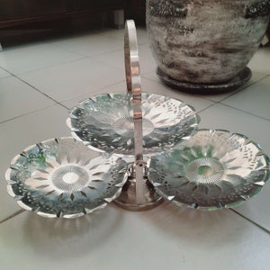 May include: A silver three-tiered serving stand with a handle. Each tier has a decorative, openwork design.