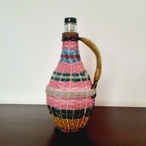 Vintage Wicker Demijohn Bottle. Glass bottle wrapped in multicolored plastic wicker. Plastic braided bottle. Old Demijohn bottle with handle
