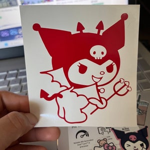 May include: Red vinyl sticker of a cartoon character with horns, a tail, and a pitchfork. The character has a skull on its head and is wearing a red hat. The character is smiling with a mischievous expression.